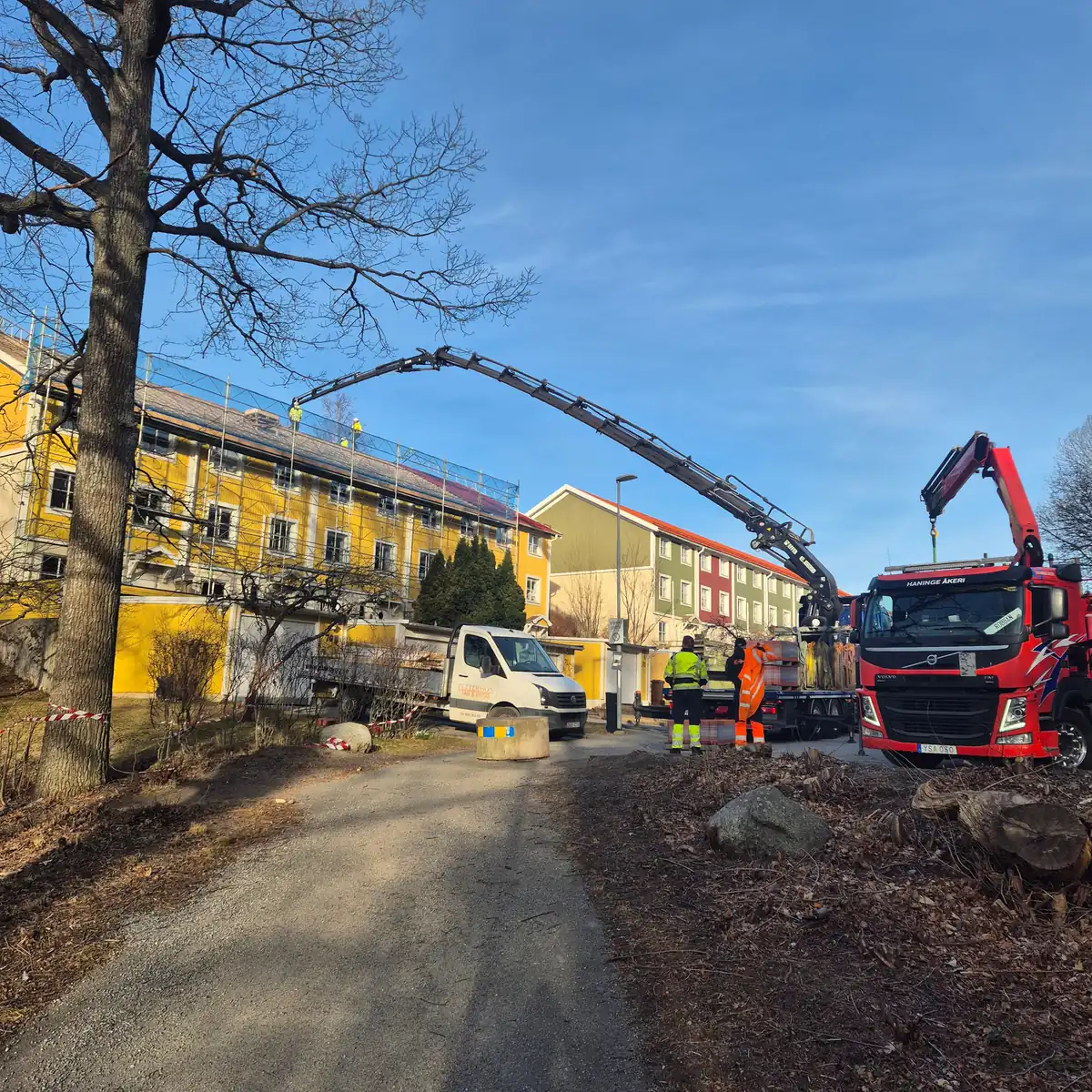 Kranbilar levererar takmaterial till ett flerbostadshus i Huddinge