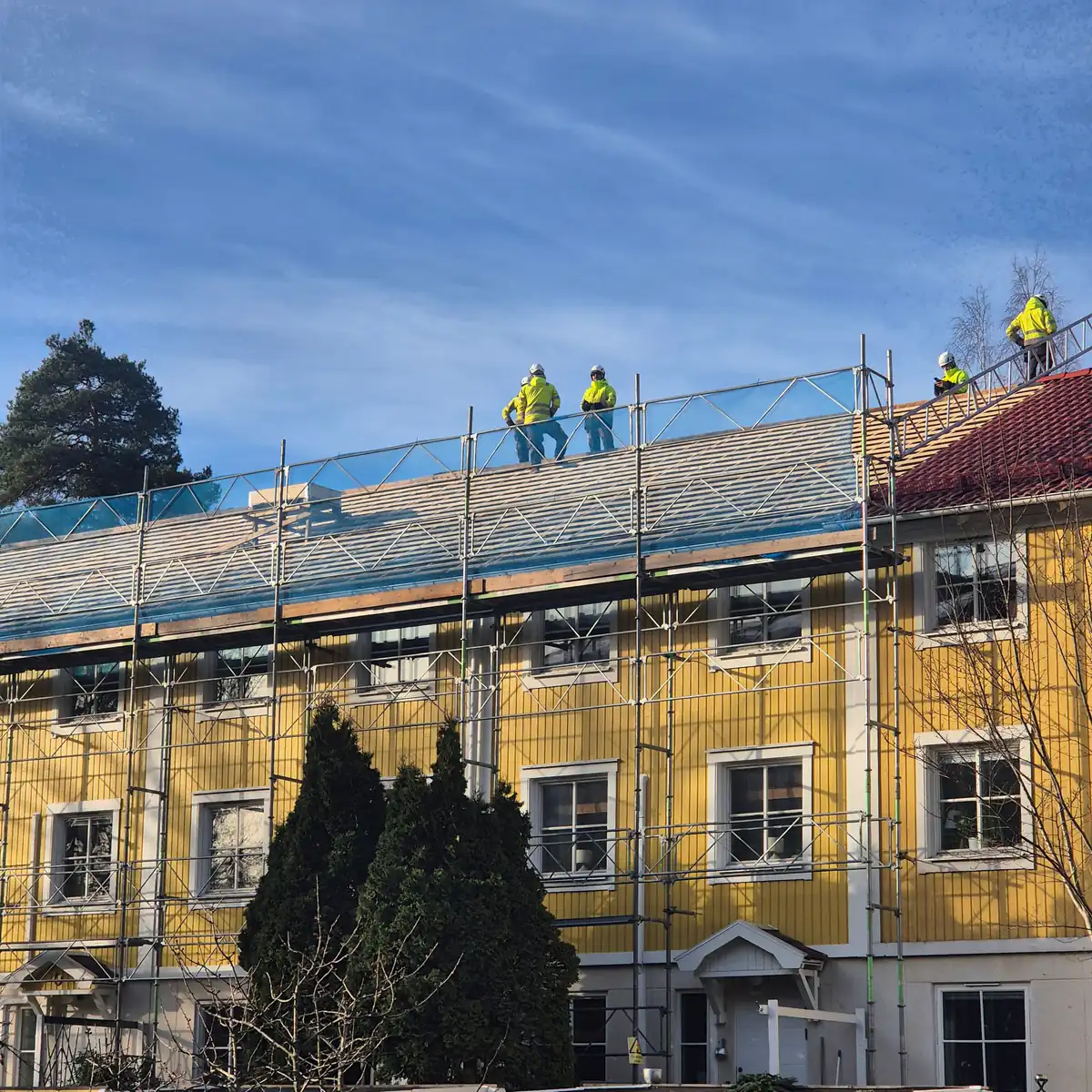 Flerbostadshus i Huddinge under takomläggning, takläggare på taket och ställning runt fasaden
