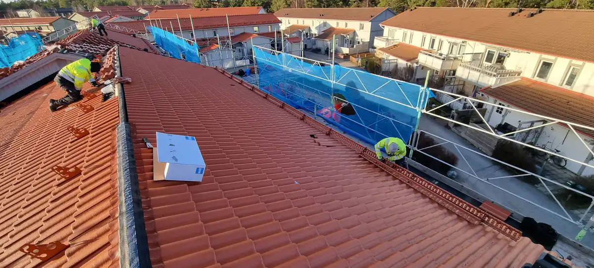 Takläggare lägger nya pannor på en radhuslänga med ställning och väderskydd