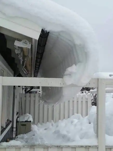 Snöhäng som rasat över takfoten på ett hus med stängsel nedanför