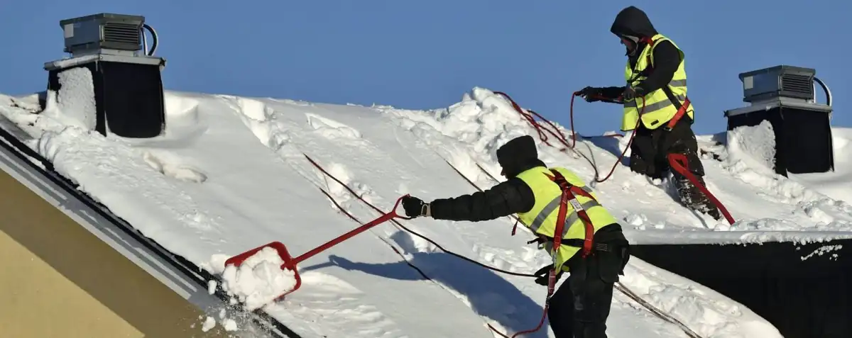 Två takskottare i sele och lina skottar snö från ett tak