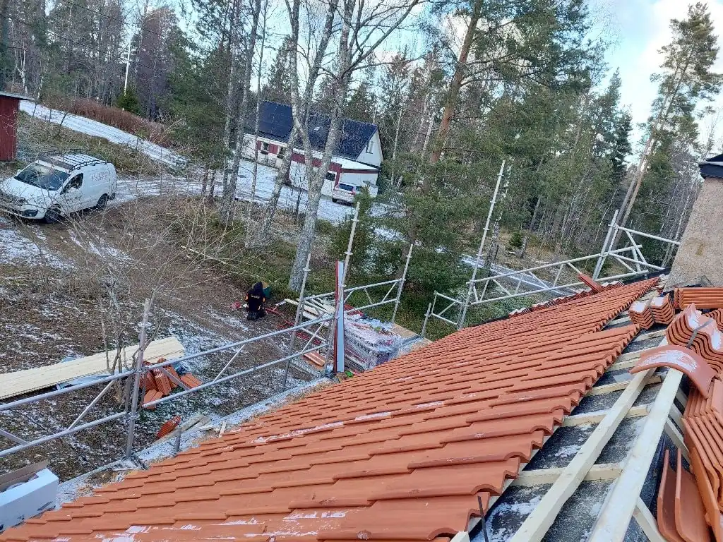 Takomläggning med lertegel i vinterväder, ställning runt huset och snö på tomten