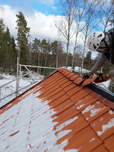 Takläggare lägger lertegel vid takfoten på ett snötäckt tak i februari